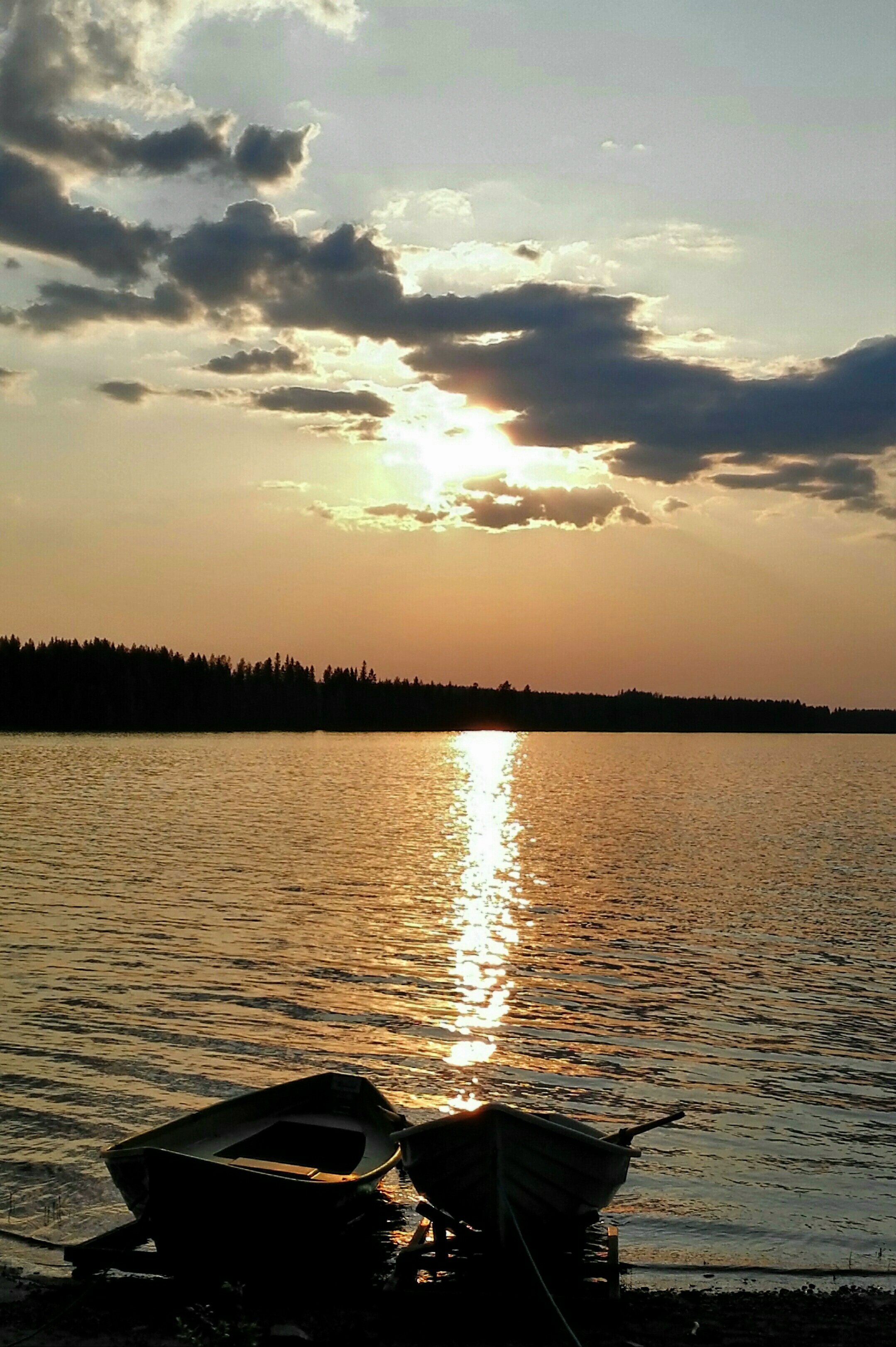 Kuvassa auringonlasku järvellä sekä kaksi venettä etualalla.